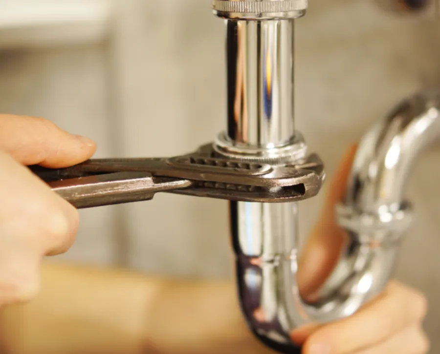 Plumber tightening a chrome sink waste pipe with a wrench